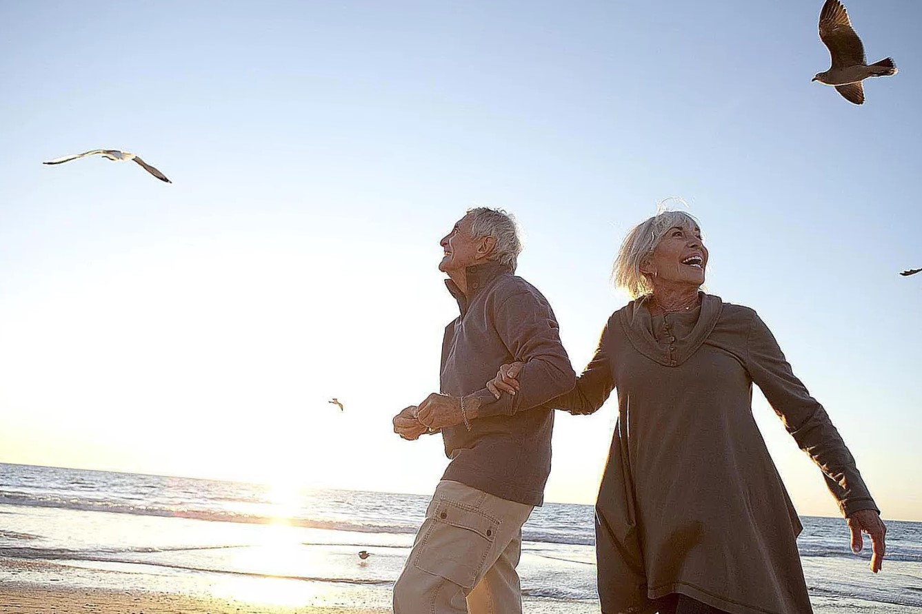 An older couple happily walking hand-in-hand along a beach, symbolizing the joy and fulfillment of retirement years.
